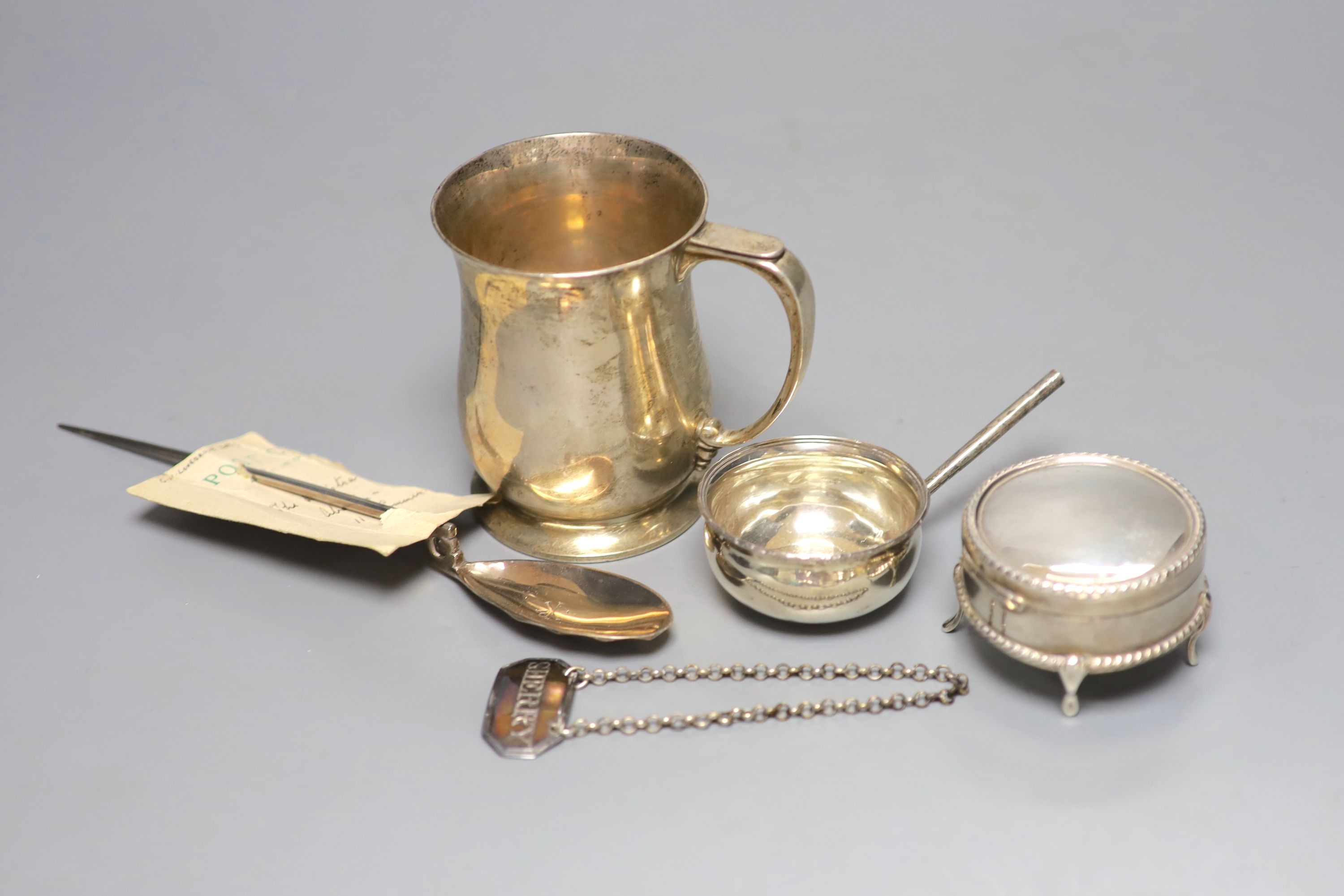 A George V silver mug, a white metal toddy ladle bowl, an Edwardian silver trinket box, a silver reproduction Roman spoon and a George III 'Sherry' label.